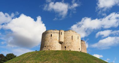 the historic stonework tower of Cliffords Tower in York, England under a sunny blue sky