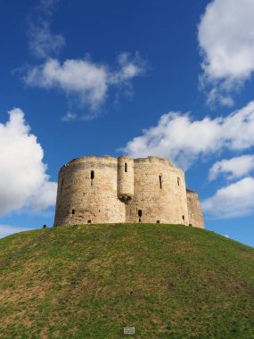 the historic stonework tower of Cliffords Tower in York, England under a sunny blue sky