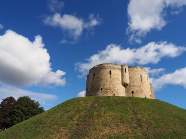 the historic stonework tower of Cliffords Tower in York, England under a sunny blue sky