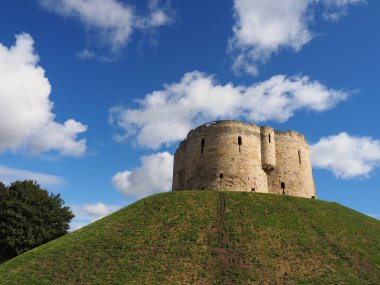 the historic stonework tower of Cliffords Tower in York, England under a sunny blue sky