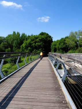 Özel bir ayak ve bisiklet köprüsü üzerinden geçen turuncu bluz ve bisiklet kaskı giyen yalnız bir bisikletçi.