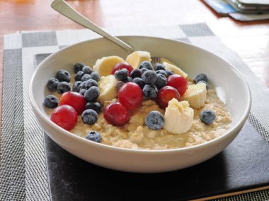 Üzerinde yaban mersini üzümü ve muz olan beyaz bir kasenin stüdyo resmi.