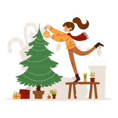 Kış kıyafetleri içinde gülümseyen bir kadının Noel ağacına hediye ve bitkilerle çevrili bir süs takması..