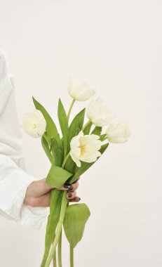 Bouquet of white tulips in a female hand on a white background. Concept gift for Valentines day, birthday, 8 March, mother day. Copy space.