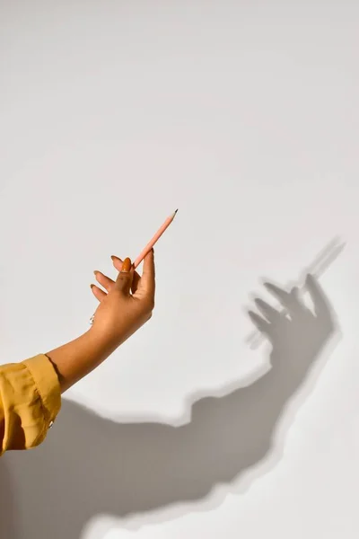 Shadow of the female hand holding a pencil,sign on the light wall. Copy space.