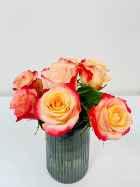 Ofiste şeffaf cam bir vazoda duran bir buket güzel gül. Beyaz arka planda izole edilmiş. Boşluğu, dokuyu, dikey fotoğrafı kopyala