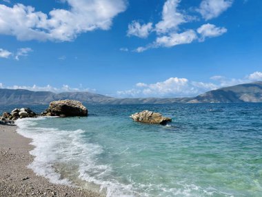 Arnavutluk 'taki Rocky plajı ve İyon Denizi' nin kristal turkuaz suyu. Çiçeklerle sakin ve rahatlatıcı bir manzara. Yaz tatili konsepti. Boşluğu kopyala.