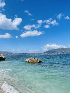 Arnavutluk 'taki Rocky plajı ve İyon Denizi' nin kristal turkuaz suyu. Çiçeklerle sakin ve rahatlatıcı bir manzara. Yaz tatili konsepti. Uzayı kopyala dikey resim 