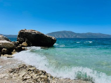 Arnavutluk 'taki Rocky plajı ve İyon Denizi' nin kristal turkuaz suyu. Çiçeklerle sakin ve rahatlatıcı bir manzara. Yaz tatili konsepti. Uzayı kopyala Yatay fotoğraf 