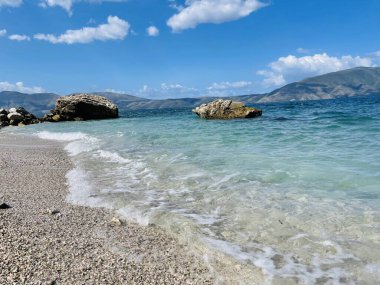 Arnavutluk 'taki Rocky plajı ve İyon Denizi' nin kristal turkuaz suyu. Çiçeklerle sakin ve rahatlatıcı bir manzara. Yaz tatili konsepti. Boşluğu kopyala.