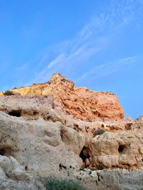 Fırtınalı bir denizden yükselen mağaraları olan yüksek kireçtaşı kayalıkları. Algar Seco, Carvoeiro Güney Portekiz, Algarve. Sahildeki kumtaşından resif oluşumu. Dikey fotoğraf. Boşluğu kopyala.