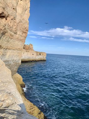 Fırtınalı bir denizden yükselen mağaraları olan yüksek kireçtaşı kayalıkları. Algar Seco, Carvoeiro Güney Portekiz, Algarve. Sahildeki kumtaşından resif oluşumu. Dikey fotoğraf. Boşluğu kopyala.