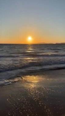 Gün batımında kumlu sahilde dalgaların gökyüzüne doğru aktığı manzara. Yüksek kaliteli FullHD görüntüler. 4K video. Korfu, Yunanistan 'daki Ada. 