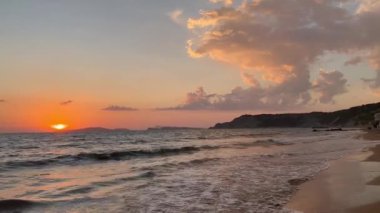 Gün batımında kumlu sahilde dalgaların gökyüzüne doğru aktığı manzara. Yüksek kaliteli FullHD görüntüler. 4K video. Korfu, Yunanistan 'daki Ada. 