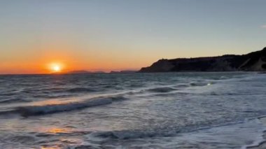 Gün batımında kumlu sahilde dalgaların gökyüzüne doğru aktığı manzara. Yüksek kaliteli FullHD görüntüler. 4K video. Korfu, Yunanistan 'daki Ada. 