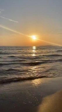 Gün batımında kumlu sahilde dalgaların gökyüzüne doğru aktığı manzara. Yüksek kaliteli FullHD görüntüler. 4K video. Korfu, Yunanistan 'daki Ada. 