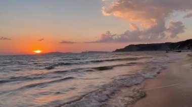 Gün batımında kumlu sahilde dalgaların gökyüzüne doğru aktığı manzara. Yüksek kaliteli FullHD görüntüler. 4K video. Korfu, Yunanistan 'daki Ada. 