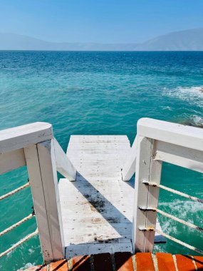 Rocky beach and crystal turquoise water of Ionian Sea in Albania. Calm and relaxing view with flowers. summer holidays concept. Copy space. clipart