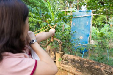 Young Woman Using Sling Shot to Shoot Target in Forest