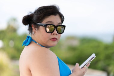 Asya Artı Boyutlu Güzel Kadın Portresi Bikini Giyiyor ve Tatil sırasında Akıllı Telefon Kullanıyor