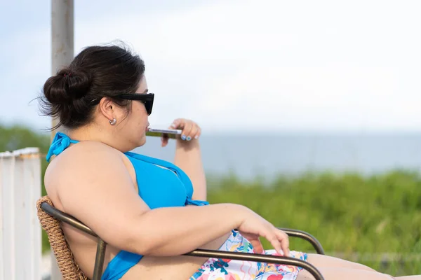 Portrait of Asian Plus Size Beautiful Woman Wearing Bikini Sitting on Chair Near Beach During Vacation
