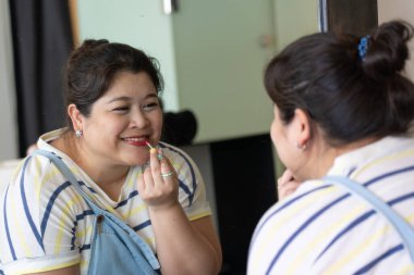 Aynaya bakan ve dudaklarına ruj süren Asyalı artı beden kadın portresi. Konumsal Vücut Şeklinin Kavramı