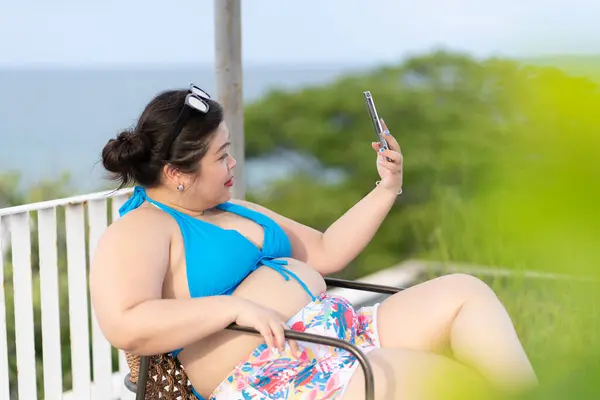 Asian Plus Soze Woman Wearing Bikini Using Mobile Phone to Selfie Herself While Vacation at Sea in Summer. Concept of Positive Body Figure.
