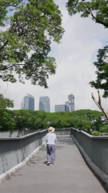 Bangkok, Tayland 'daki Benjakitti Parkı' nda Kıdemli Asyalı Kadın Köprüde Yürüyor. Dikey Görüntü 
