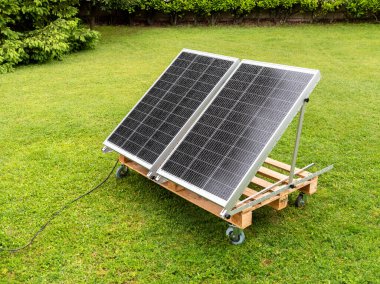 Yağmurdan ıslanan fotovoltaik paneller ev bahçesindeki ahşap paletin üzerinde. Yeşil enerji kavramı.