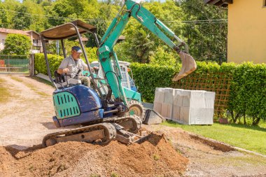 Mini kazıcıda çalışan bir işçi evin önünü kazıyor. Zemin ve dış döşeme.