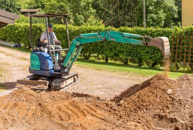 Mini kazıcıda çalışan bir işçi evin önünü kazıyor. Zemin ve dış döşeme.