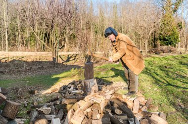 Üst sınıftan bir adam bahçede baltayla sandığı yakacak oduna ayırıyor..