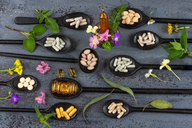 Kapsüller ve diyet ilaveleri etrafını çiçekler ve tıbbi bitkiler sarmış..
