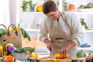Mutfağında organik sebzelerle çevrili genç bir kadın var.