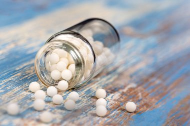 Homeopati: hafif bir arka planda küçük çiçekler arasında yayılan homeopatik granüllerin yakın çekimi.