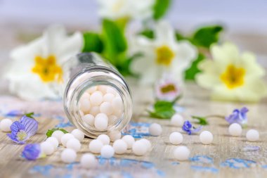 Homeopati: hafif bir arka planda küçük çiçekler arasında yayılan homeopatik granüllerin yakın çekimi.
