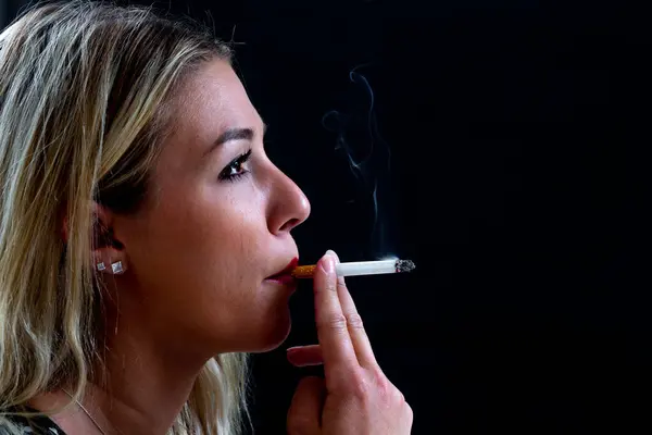 在黑色背景下吸烟的年轻女子的特写镜头 制造了滚滚浓烟 图库图片