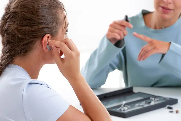 在听力护理专业人员面前测试助听器的妇女 图库照片