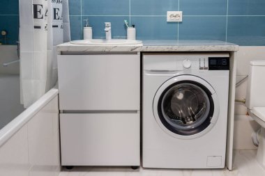 Tezgahında lavabo ve tezgahın altında çamaşır makinesi olan bir banyo.