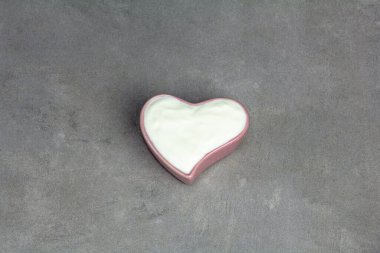 Yogurt in heart shaped bowl, top view on gray concrete background