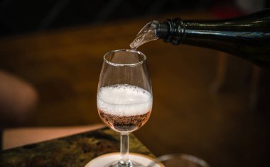 Bir şişeden beyaz köpüklü şarap bir cam kadehe dökülür. Şarap arıtma. Yakın plan..