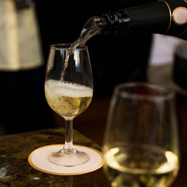 Bir şişeden beyaz köpüklü şarap bir cam kadehe dökülür. Şarap arıtma. Yakın plan..