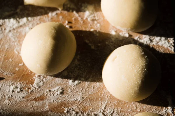 Close-up of raw dough balls and flour on wooden counter. Ready for baking. Sunlight.
