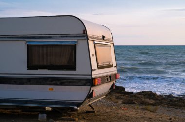 Karavan deniz kıyısına park etmiş. Suda dalgalar. Vahşi kamp yeri manzarası. Seyahat et. Tatilde. Gün batımı ışığı.