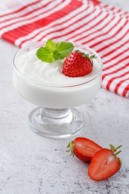 Sütlü puding ya da çilekli yoğurt ve cam kaptaki naneli yapraklar, arka planda. Sağlıklı vitaminler ve mineral gıdaları.