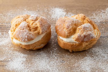 Kremalı pasta, choux 'un yaptığı hamur tatlısı ahşap masanın üzerinde şeker tozu. Kahve molası ya da parti için tatlı tatlı.