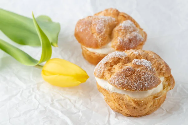 奶油泡芙 用苏打粉做的糕点和白纸上的黄色郁金香花 喝咖啡休息或聚会的甜食 — 图库照片