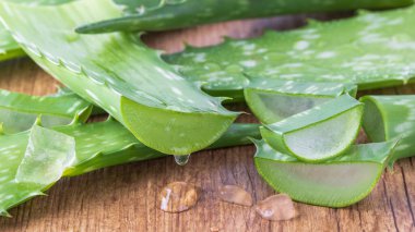 Ahşap tahtaya dilimlenmiş saf aloe vera yaprağından damlayan meyve suyu. Dilimlenmiş aloe vera yaprakları ve yakın plan jel damlaları. Sağlıklı gıda ve doğal cilt bakımı bileşeni.