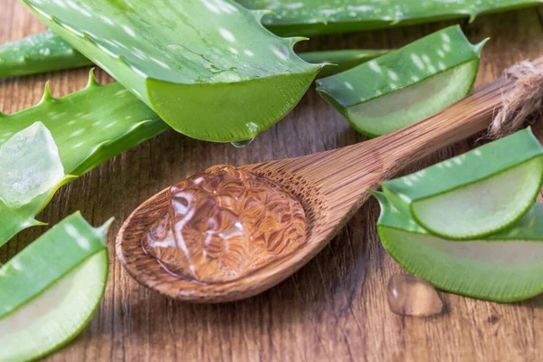 Ahşap kaşıkta dilimlenmiş saf aloe vera yaprağından damlayan meyve suyu. Dilimlenmiş aloe vera yaprakları ve yakın plan jel damlaları. Sağlıklı gıda ve doğal cilt bakımı bileşeni.