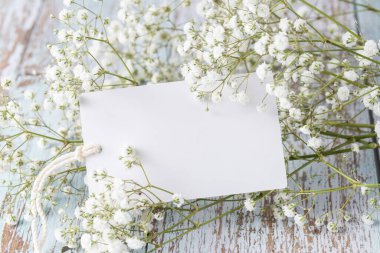 Boş kartıyla düğün modeli ve eski ahşap arka planda beyaz çigila çiçekleri. Fotokopi alanı olan çiçek çerçevesi. Üst görünüm karşılama kompozisyonu.